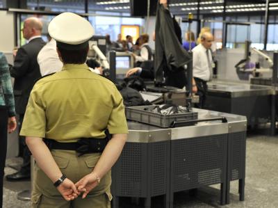 Unter den Augen einer Polizistin warten Passagiere auf die Kontrolle ihres Handgepäcks. (Archivfoto) Kontrolle