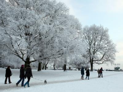 Spaziergänger gehen durch einen mit Schnee bedeckten Park in Hamburg. Schneefall und Kälte bestimmen seit Tagen das Wetter in der Hansestadt. Park in Hamburg