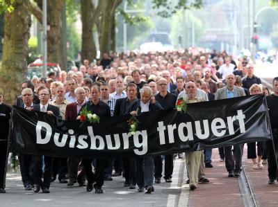 Teilnehmer eines Trauermarsches ziehen in Duisburg nach einem improvisierten Gottesdienst zur Unglücksstelle. Trauerfeier Loveparade