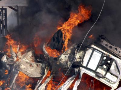 Flammen schlagen aus dem Wrack eines Wagens. Autobombenanschlag