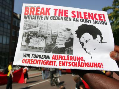 Demonstranten wenden sich mit einem Plakat gegen die ihrer Meinung nach schleppende Aufklärung des Feuertodes von Oury Jalloh. (Archivbild) Demonstration