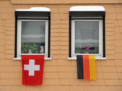 Eine deutsche und eine Schweizer Flagge an den Fenstern eines Hauses. Fahnenschmuck