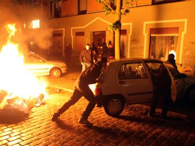 Passanten schieben im Hamburger Schanzenviertel ein Auto von einer brennenden Barrikade weg. Mai-Krawalle