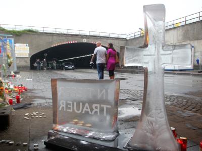 Ein Kreuz mit einer Gedenktafel aus Eis taut in Duisburg an der Unglücksstelle der Loveparade auf. Trauer