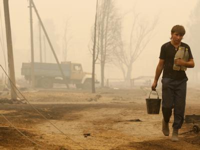 Ein Junge mit Wasserflaschen in einem von den Flammen zerstörten Dorf in Russland. Verbrannt