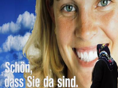 Eine Frau mit Kopftuch vor einem Werbeplakat in Berlin. Foto: Johannes Eisele/Archiv Migranten in Deutschland