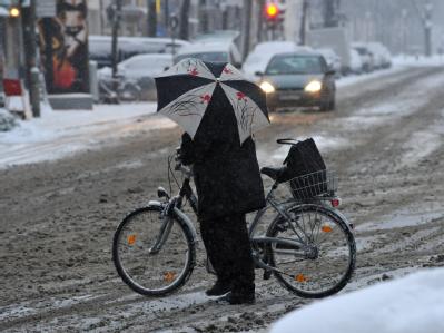 Erschwerte Bedingungen: Eine Frau schiebt am Montagmorgen ihr Fahrrad über eine verschneite Kreuzung in München. Schneefall in München