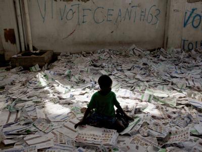 Ein Kind sitzt zwischen den Wahlzetteln in einem Flüchtlingslager in Haitis Hauptstadt Port-au-Prince. Nach Chaoswahlen in Haiti