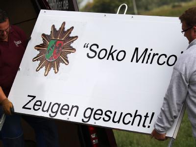 Mitarbeiter einer Schilderfirma stellen ein Plakat der Polizei auf. 'Zeugen gesucht'