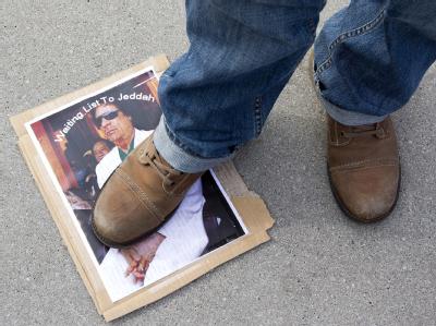 Ein Demonstrant in Genf steht auf einem Foto von Muammar al-Gaddafi. Demo in Genf
