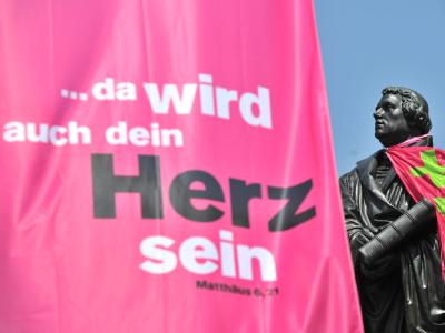 Eine Fahne mit dem Motto des Evangelischen Kirchentages neben einer Statue von Martin Luther. Kirchentag