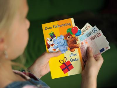Ein Kind entnimmt Geldscheine aus einem Geburtstagsbrief. (Symbolbild) Hartz IV-Kürzung wegen Omas Geburtstagsgeld?