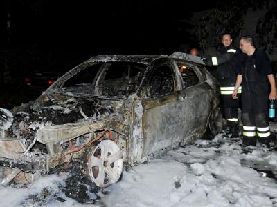 Feuerwehrleute untersuchen ein ausgebranntes Fahrzeug auf einem Parkplatz am Berliner Gesundbrunnen. Autozündeleien in Berlin gehen weiter