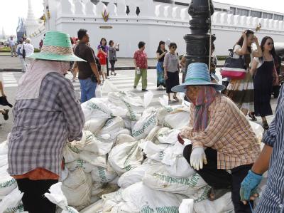 Touristen schauen zu, wie Anwohner Bangkoks vor dem Großen Palast Sandsäcke auftürmen. Foto: Barbara Walton, dpa Bangkok