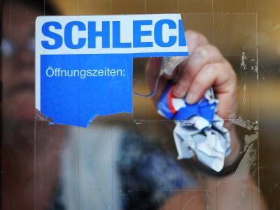 Eine Mitarbeiterin von Schlecker reißt das Firmenlogo von der Eingangstür einer Filiale. Foto: Julian Stratenschulte Schlecker
