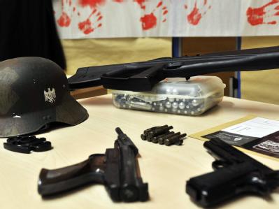 Ein sichergestellter Helm mit Hakenkreuz, ein Schlagring, zwei Pistolen, die Nachbildung eines Gewehrs und Patronen sind nach einer Razzia gegen die rechte Szene im Polizeipräsidium Köln zu sehen. Foto: Marius Becker Razzia in der rechten Szene