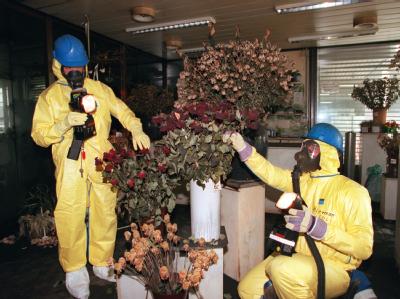 Zwei Feuerwehrleute in Schutzanzügen inspizieren am 11.07.1996 das mit giftigen Dioxin-Stäuben verseuchte Blumengeschäft am Düsseldorfer Flughafen. 17 Menschen starben hier. Foto: Martin Gerten Brandkatastrophe in Düsseldorf