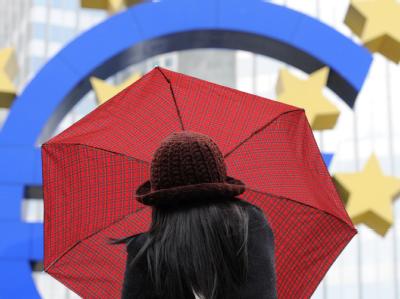 Eine Frau spannt bei regnerischem Wetter vor der Euro-Skulptur in Frankfurt am Main ihren Regenschirm auf. Foto: Arne Dedert/Archiv Rettungsschirm