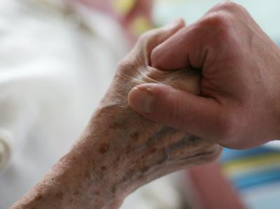 Ein Pfleger hält die Hand einer alten, kranken Frau. Foto: Oliver Berg / Archiv Sterbehilfe