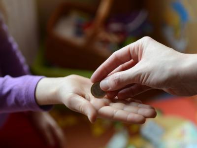 Ein Mädchen erhält von der Mutter einen Euro Taschengeld. Foto: Jens Kalaene Taschengeld