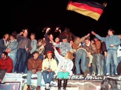 Jubelnde Menschen freuen sich 1989 auf der Berliner Mauer über die Öffnung der deutsch-deutschen Grenzen. Berliner Mauer