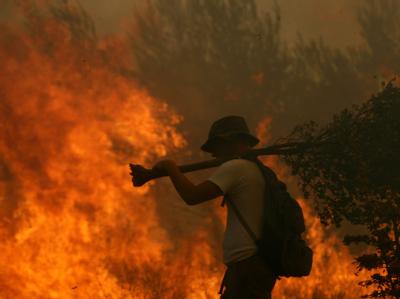 Ein freiwilliger Helfer der Feuerwehr vor einer Flammenwand. Waldbrand