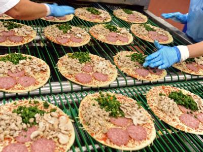 Tiefkühlpizzen vom laufenden Band. Oft wird auf Pizzen Schummelkäse verwendet. Pizza-Produktion