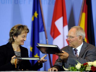 Bundesfinanzminister Wolfgang Schäuble (CDU) und die Schweizer Bundesrätin Eveline Widmer-Schlumpf tauschen nach der Unterzeichnung des Steuerabkommens im Jahr 2011 die Mappen aus. Foto: Soeren Stache/Archiv Steuerabkommen