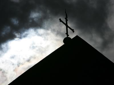 Im Gegenlicht und vor wolkenverhangenem Himmel: Eine Kirchturmspitze mit Kreuz. Foto: Friso Gentsch Kreuz im Gegenlicht