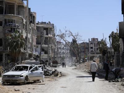 Menschen gehen an zerstörten Häusern und Autos im syrischen Duma vorbei. Foto: Hassan Ammar/AP Duma