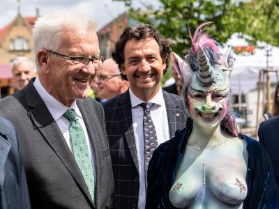 Winfried Kretschmann, Ministerpräsident von Baden-Württemberg, steht neben der als Einhorn maskierten Cynthia Schneider (Die Linke). Eröffnung Remstal Gartenschau