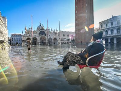 Eine Frau sitzt auf einem Stuhl im Hochwasser auf dem Markusplatz. Platz im Wasser