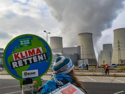 Eine Aktivistin protestiert vor den dampfenden Kühltürmen des Kraftwerks Jänschwalde in der Lausitz gegen die Braunkohle-Verstromung. Protest in Brandenburg