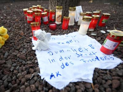 Am Königsplatz liegt eine Engelsfigur auf einem Stück Stoff, auf dem steht ?Ein Toter wegen Dummheit! In der Stadt des Friedens!?. Trauer in Augsburg