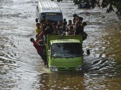 Menschen stehen auf der Ladefläche eines Transporters, um eine überflutete Straße in Jakarta zu passieren. Überschwemmungen in Indonesien