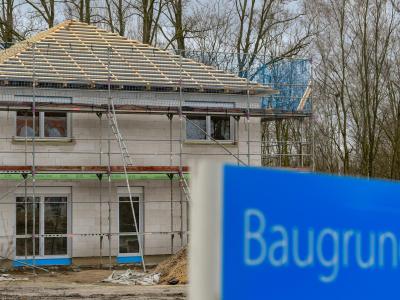 Ein Schild mit der Aufschrift «Baugrundstücke» steht am Rande eines Baufeldes mit einem Rohbau eines Eigenheimes. Rohbau