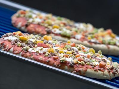 Tiefgefrorene Pizzen laufen über ein Transportband. Tiefkühlkost