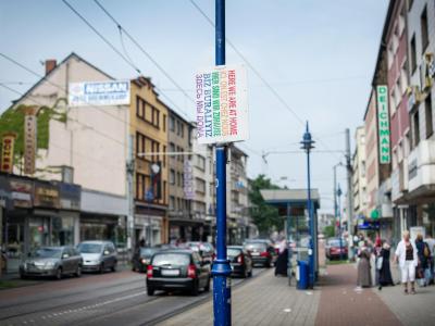 Ein Schild «Hier sind wir zuhause» in verschiedenen Sprachen hängt in Duisburg auf der Straße. Duisburg-Marxloh