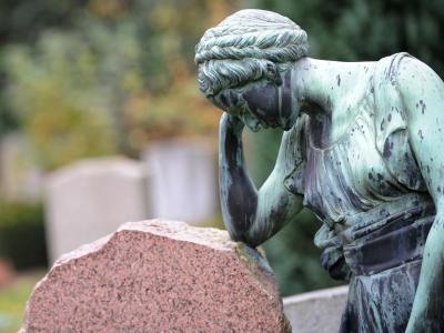 Eine Frauenfigur lehnt an einem Grabstein. Friedhof