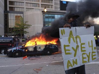 Ein Demonstrant hält bei einer Protestaktion in der Nähe eines brennenden Polizeiautos ein Schild mit dem Anfang eines Zitats aus der Bibel «Auge um Auge». Demonstrant