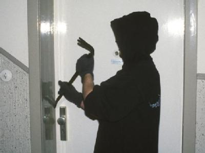 Ein vermummter Einbrecher macht sich mit einem Brecheisen an einer Wohnungstür zu schaffen. Foto: dpa/Symbolbild Wohnungseinbruch
